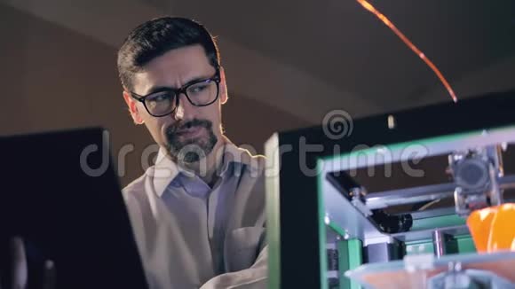 一位带笔记本电脑的工程师正在工作中观看3D打印机视频的预览图