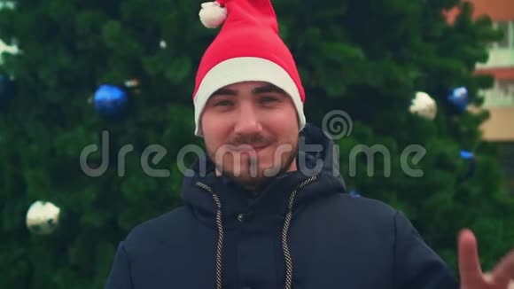 快乐英俊的男人的肖像戴着圣诞老人的帽子穿着黑色夹克自信地看着相机微笑着视频的预览图