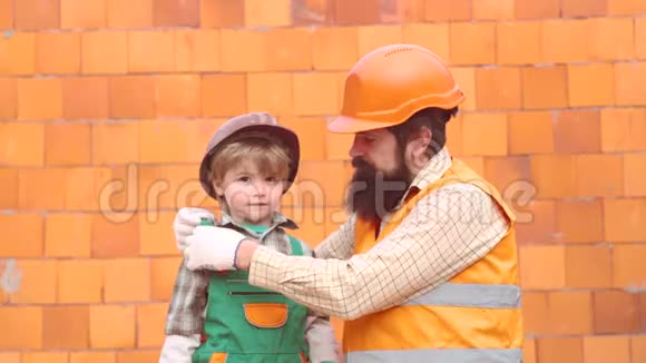 儿子和父亲放一块砖来建一堵墙男孩扮演建筑工或修理工父亲和孩子在家一起帮忙视频的预览图