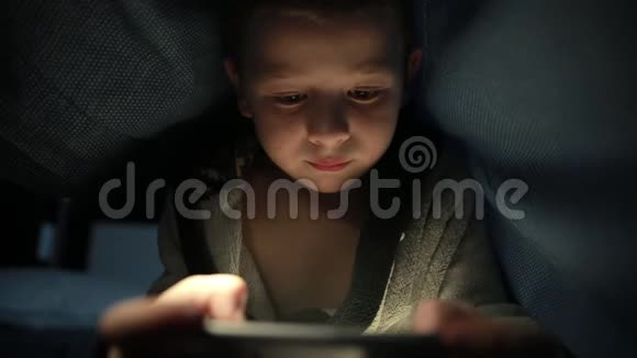 毯子下面的小家伙晚上在他的手机智能手机上玩游戏视频的预览图