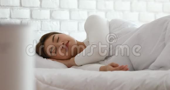 女人在舒适的白色卧室里与空气净化器一起睡觉用于过滤和清洁去除灰尘PM25HEPA在家里视频的预览图
