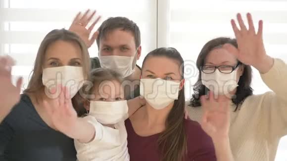 五口之家佩戴防护医疗口罩预防冠状病毒大人和孩子挥手视频的预览图