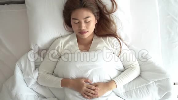 美丽迷人的亚洲女人穿着睡衣睡觉闭上眼睛微笑着睡觉在卧室的床上做着甜蜜的梦视频的预览图