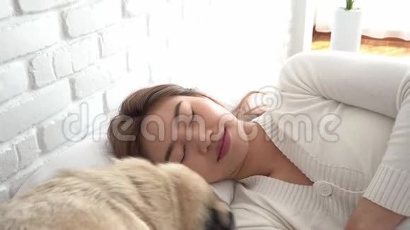 穿着睡衣睡觉的亚洲女人闭上眼睛微笑着睡觉狗在卧室里醒着视频的预览图