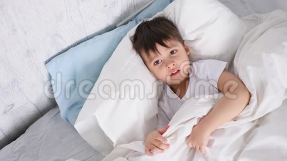 躺在白色床上的孩子躲在家里的毯子下面视频的预览图