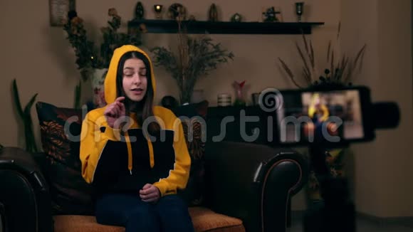 一个年轻的欧洲女孩坐在家里的扶手椅上在手机上录制视频并要求订阅视频的预览图