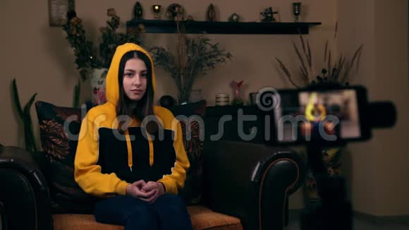 一位欧洲貌美的年轻女孩坐在家里的扶手椅上在手机上录制视频视频并大拇指视频的预览图