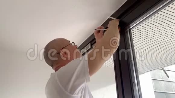 戴着中年眼镜的秃头男子正在房间窗户上拧着飞檐螺丝这是男性家庭作业修理的概念视频的预览图