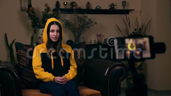 一位欧洲貌美的年轻女孩坐在家里的扶手椅上在手机上录制视频视频并大拇指视频的预览图
