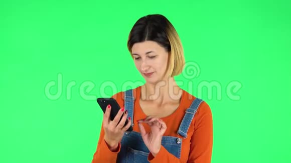 年轻女子在手机上自拍然后在绿色屏幕上看照片视频的预览图