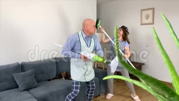秃顶的男人和女人穿着家里的衣服和围裙用吸尘器欢快地跳舞模仿弹吉他视频的预览图
