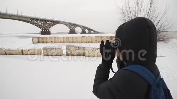 一个女孩在河边拍摄冬天的风景女摄影师在城市的桥边拍照视频的预览图