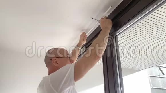 戴着中年眼镜的秃头男子正在房间窗户上拧着飞檐螺丝这是男性家庭作业修理的概念视频的预览图