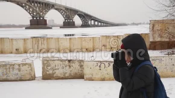 冬天一个女孩在一条结冰的河上拍摄一座桥女摄影师在大自然中拍照视频的预览图
