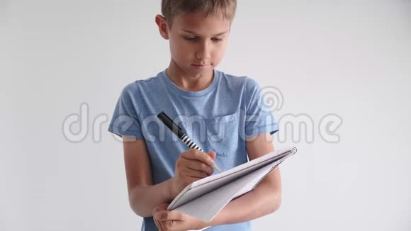 十几岁的男孩站着手里拿着螺旋式学校作业本笔记本用钢笔写笔记视频的预览图