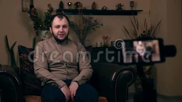 这位颇具影响力的留胡子年轻人一位来自欧洲的博客作者穿着衬衫坐在椅子上拍摄视频视频的预览图