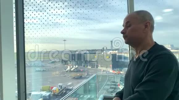 一名男子坐在机场休息室明亮的大楼里在窗口等候看着街道旅行理念视频的预览图