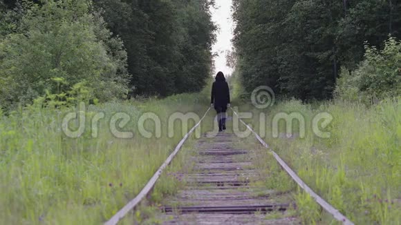 一个孤独的黑衣人走在树林里的铁轨上后景他感到轻松思考和无聊视频的预览图