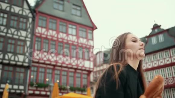 穿着黑色夹克衫的德国女孩笨拙地手底下拿着纸包的面包视频的预览图