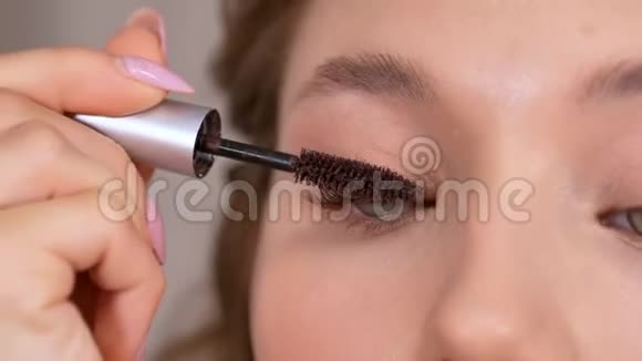 化妆年轻女孩看着镜子用刷子在眼睛的睫毛上涂上睫毛膏视频的预览图
