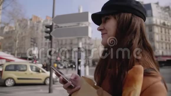 快乐迷人的年轻女子微笑着在秋天阳光明媚的巴黎街慢动作上阅读智能手机上的信息视频的预览图