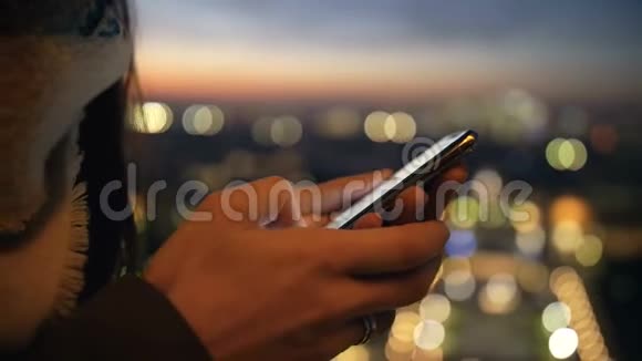 美丽的特写镜头女性手使用智能手机购物应用程序在惊人的bokeh日落城市灯光风景慢动作视频的预览图