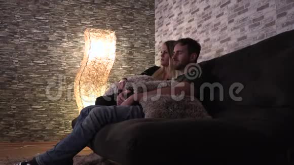爱的一对夫妇在大厅里沙发上拥抱着看电视视频的预览图