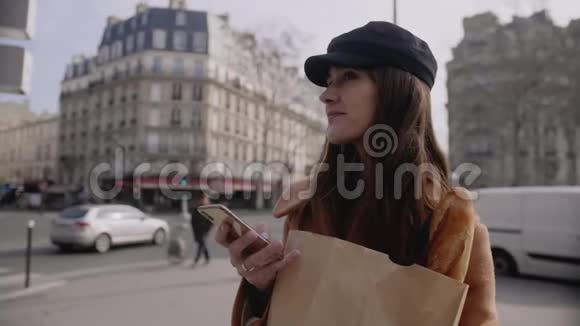 快乐美丽的年轻博主女士四处寻找在阳光明媚的巴黎街慢动作上使用智能手机在线发布视频的预览图