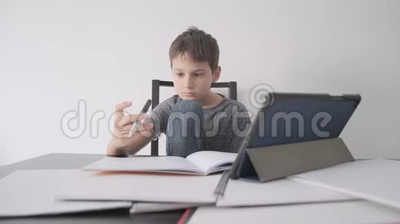 悲伤的孩子坐在桌子上拿着平板电脑和许多书男孩感到无聊因为他不懂作业视频的预览图