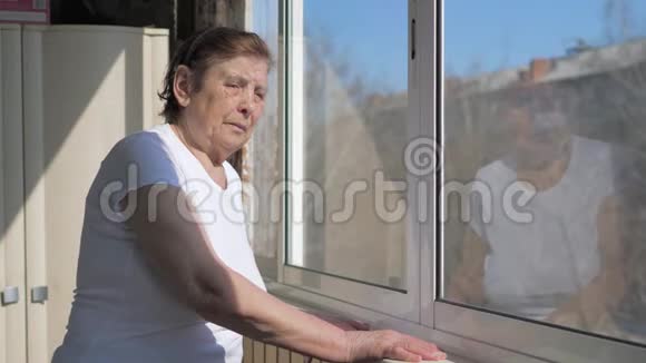 一位老妇人站在窗边在晴朗的天气看着外面视频的预览图
