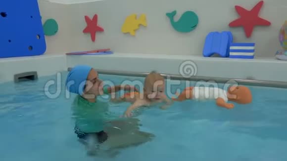 母亲用双手托着婴儿这是漂浮在孩子们水池水中宝宝游过去视频的预览图