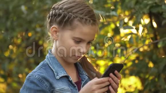 十几岁的女孩独自在苹果花园的背景下使用手机智能手机成瘾视频的预览图
