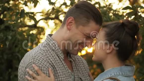 快乐的男人和女孩在公园日落时亲吻和拥抱在苹果园浪漫的环境中爱男人和女人视频的预览图