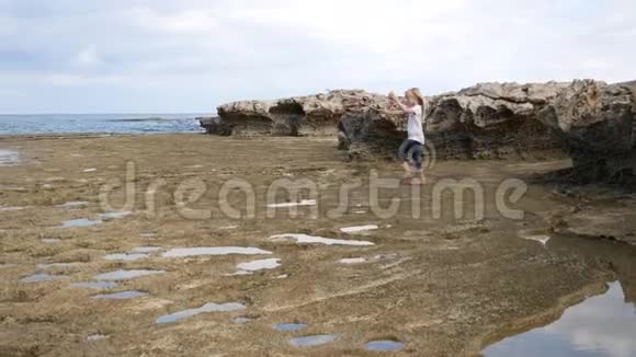 一个女孩走在岩石海岸看着水坑寻找有趣的东西视频的预览图