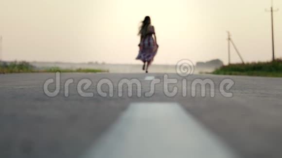 一个漂亮的年轻的女孩穿着一件长裙子赤脚在路上奔跑她快乐而无忧无虑动作缓慢模糊视频的预览图