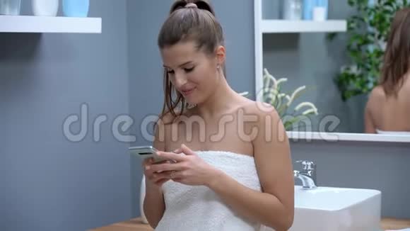 早上在浴室里使用智能手机的快乐成年女性视频的预览图