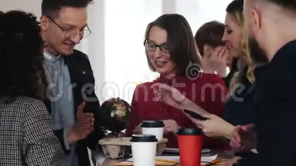 快乐多样的商业团队站在一起在桌子上旋转小地球在办公室休息时微笑和聊天视频的预览图