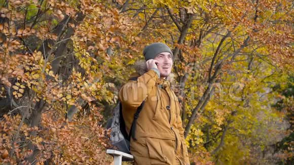 年轻的男游客戴着一顶帽子穿着一件背包在智能手机上微笑着在背景下欢欣鼓舞视频的预览图