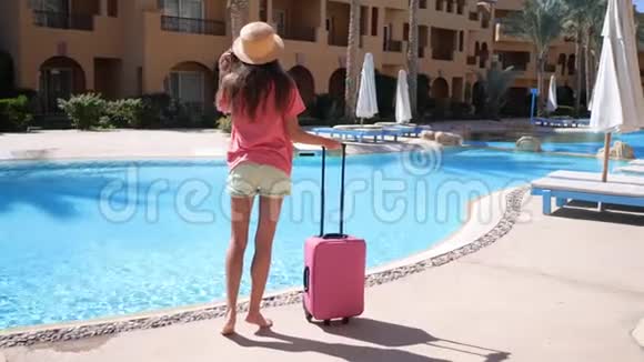 带粉红色箱子的年轻女子住在酒店的游泳池附近旅游度假概念高清视频支持1920x1080视频的预览图