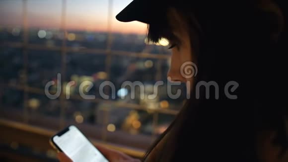 侧景特写年轻漂亮的女人用智能手机在玻璃建筑墙上与bokeh日落视图慢动作视频的预览图