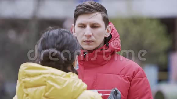 一位年轻的欧洲女性在户外给她的男朋友戴上一次性医用口罩新冠状病毒COVI视频的预览图