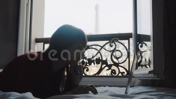 快乐美丽的白种人女商人使用笔记本电脑躺在法国房间阳台的床上享受假期慢动作视频的预览图