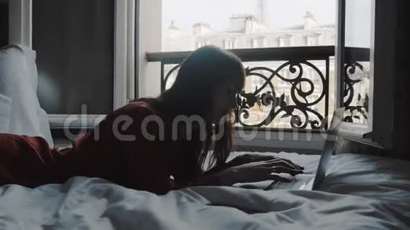 快乐美丽的黑发作家女士在笔记本电脑上打字躺在床上看着美丽的埃菲尔铁塔景慢动作视频的预览图