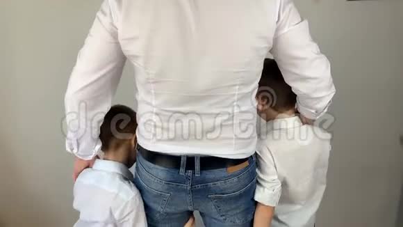 穿着白色衬衫的年轻人拥抱他的两个小儿子一个好家庭的概念背着他站着视频的预览图