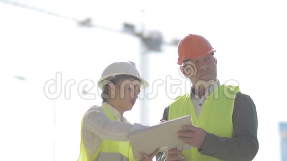 两位建筑工人一男一女正在讨论工作问题在起重机的背景下视频的预览图