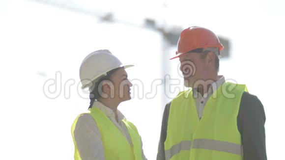 两位建筑工人一男一女正在讨论工作问题在起重机的背景下视频的预览图
