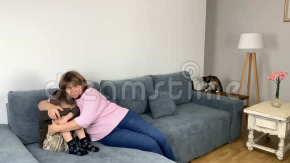 女人母亲用手臂拥抱她的儿子孩子坐在沙发上家庭教育的概念和视频的预览图