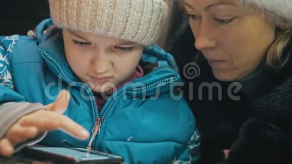 漂亮的白种人母女使用智能手机坐在咖啡馆里高级幼儿表演和讲解视频的预览图