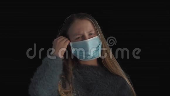 可爱生病的女孩打喷嚏生病的女孩戴着医疗面罩一个生病的女孩在黑色背景的医疗面具上的肖像咳嗽视频的预览图