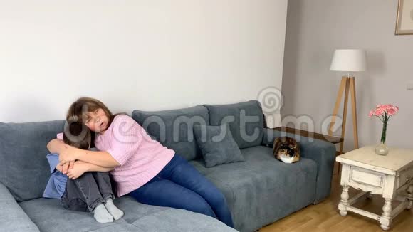 孩子一个穿牛仔裤的小学男孩一件蓝色衬衫坐在沙发上遮住他的脸妈妈坐在附近拥抱她的儿子视频的预览图